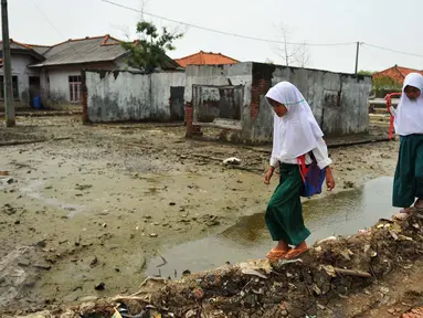 Dua orang siswi melewati pelataran bekas rumah yang terkena dampak abrasi di pantai Muara Gembong, Bekasi, Selasa, (26/7). Tingkat abrasi yang tinggi menyebabkan sejumlah rumah terkikis dan beberapa sekolah terendam air laut. (Liputan6.com/Gempur M Surya)