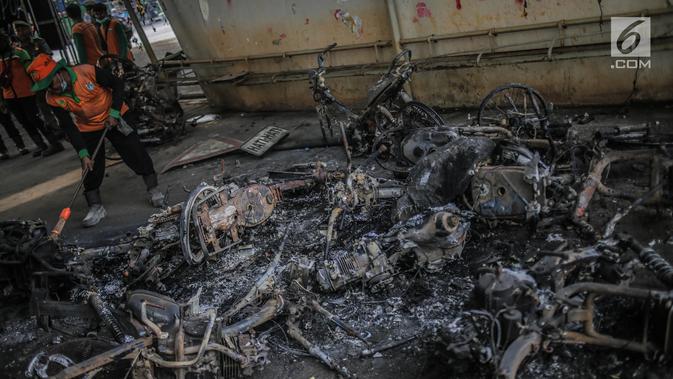 Petugas mengumpulkan bangkai sepeda motor yang dibakar massa aksi di bawah jembatan layang Slipi, Jakarta, Kamis (26/9/2019). Aksi menolak revisi UU KPK, revisi UU KUHP dan sejumlah revisi UU lainnya berjalan anarkis di sekitar Gedung DPR pada Rabu 25 September 2019. (Liputan6.com/Faizal Fanani)