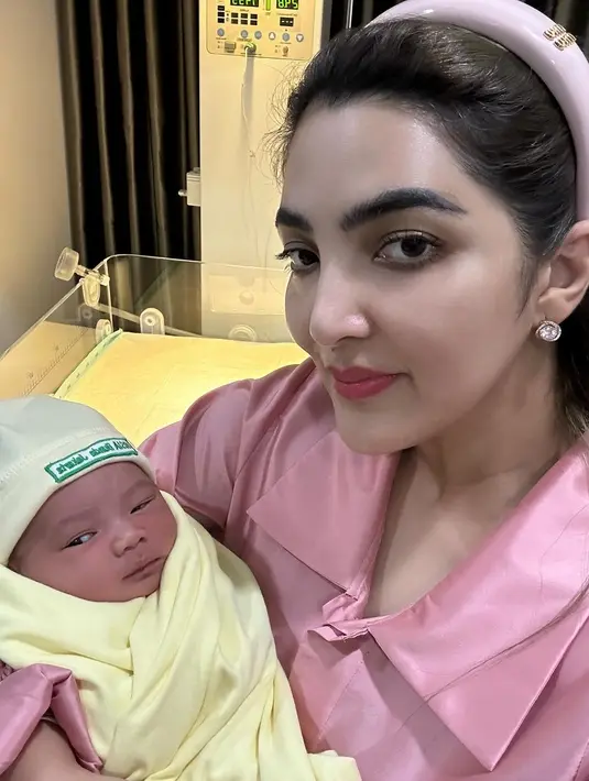 Di beberapa foto terbaru, Ashanty memamerkan gayanya saat menggendong cucu keduanya dari Aurel dan Atta. Mengenakan atasan berkerah berwarna merah muda dari bahan satin, Ashanty tampil kasual dengan rambut dibando yang juga berwarna pink. [Foto: Instagram/ashanty_ash]