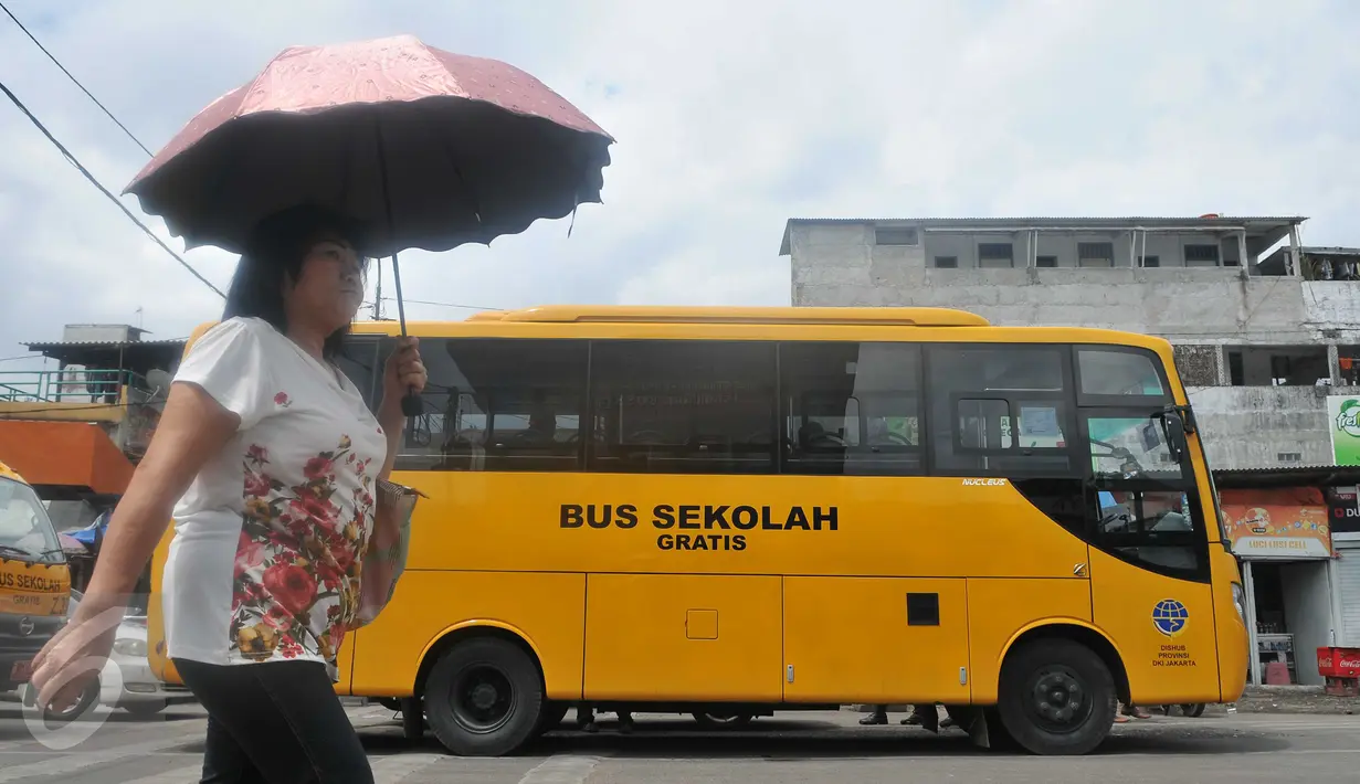 Seorang warga melintas di depan Bus Sekolah di Terminal Senen, Jakarta, Senin (21/12/2015). Bus sekolah menggantikan Metro Mini yang melakukan aksi mogok karena takut terkena razia Dishub. (Liputan6.com/Gempur M Surya)