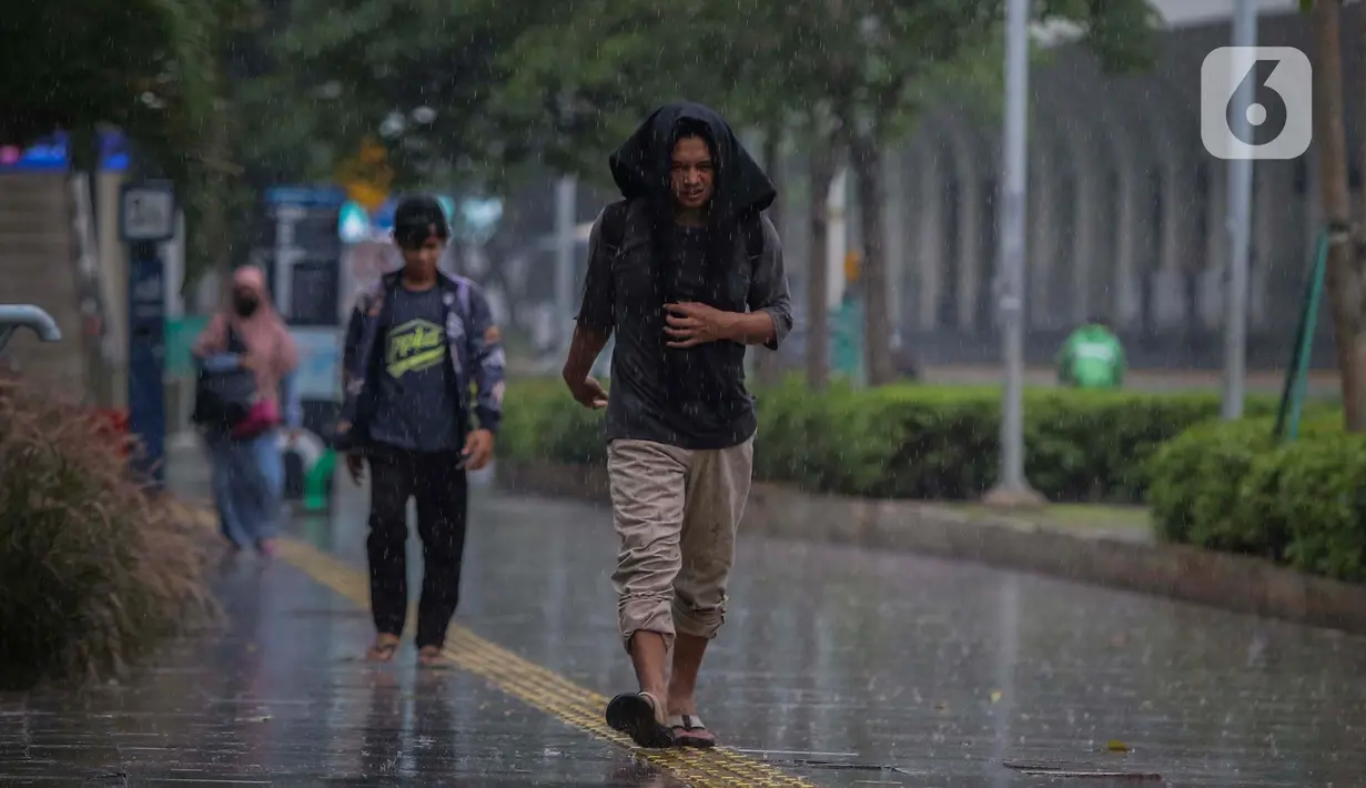 Warga menutupi kepala dari guyuran hujan saat melintasi kawasan Sudirman, Jakarta, Kamis (4/1/2024). (Liputan6.com/Angga Yuniar)