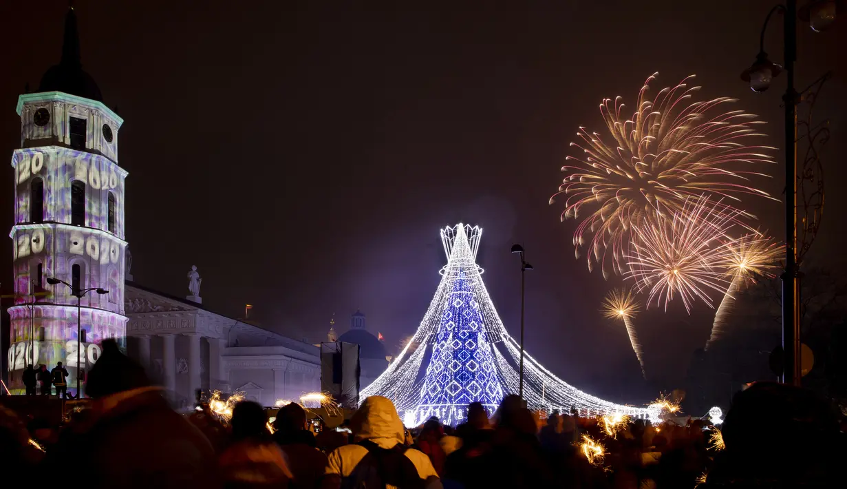Kembang api menerangi langit di atas pohon Natal yang menyala di Lapangan Katedral di Vilnius, Lithuania selama perayaan Tahun Baru, Rabu (1/1/2020). (AP Photo/Mindaugas Kulbis)