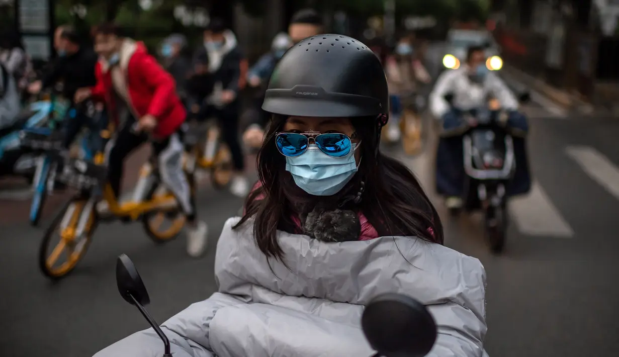 Seorang perempuan yang memakai masker untuk mengurangi risiko tertular virus corona COVID-19 bepergian dengan sepeda listrik selama jam sibuk di Beijing, China pada 14 Oktober 2020. (Photo by NICOLAS ASFOURI / AFP)