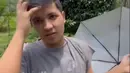 Penampilannya begitu sederhana dengan kaos abu-abu longgar dan celana hitam santai. Sambil berjalan di antara pepohonan karet, Jirayut menunjukkan bagaimana proses penyadapan getah dilakukan. Sesekali, ia bercanda dengan menunjukkan wadah kecil berisi getah karet, membuat suasana terasa akrab dan ceria. (Liputan6.com/IG/@jirayutdaa4official)