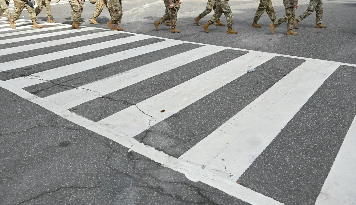 Anggota Garda Nasional menyeberang jalan di Washington, DC, saat pengamanan diperketat pada Senin (18/1/2021). Menurut laporan, 25.000 tentara Garda Nasional akan menjaga kota tersebut sebagai persiapan untuk pelantikan Joe Biden sebagai Presiden ke-46 Amerika Serikat. (Brendan Smialowski/AFP)