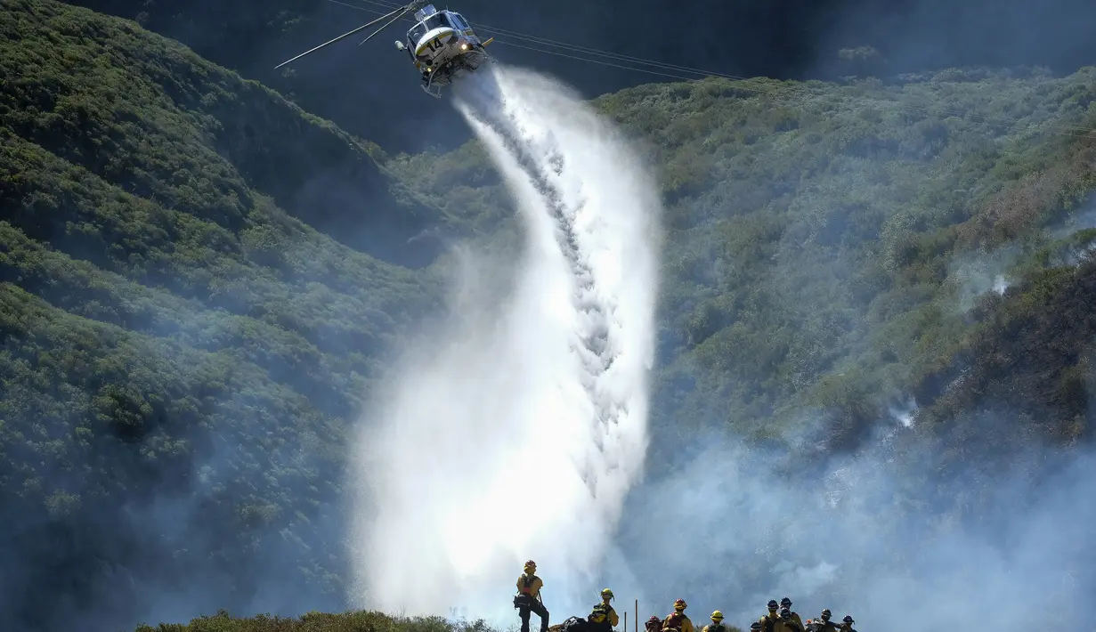 Petugas pemadam kebakaran menyaksikan helikopter menjatuhkan air pada kebakaran hutan di Laguna Beach, California, Kamis (10/2/2022). Kebakaran hutan yang dipicu oleh angin kencang Santa Ana meletus di perbukitan di pantai California Selatan Kamis pagi. (AP Photo/Ringo H.W. Chiu)