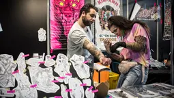 Seorang seniman tato wanita memeriksa tangan pelanggannya untuk di tato saat acara Konvensi Tattoo Paris (Mondial du Tatouage) di Grand Halle de la Villette di Paris (8/3). (AFP/Philippe Lopez)