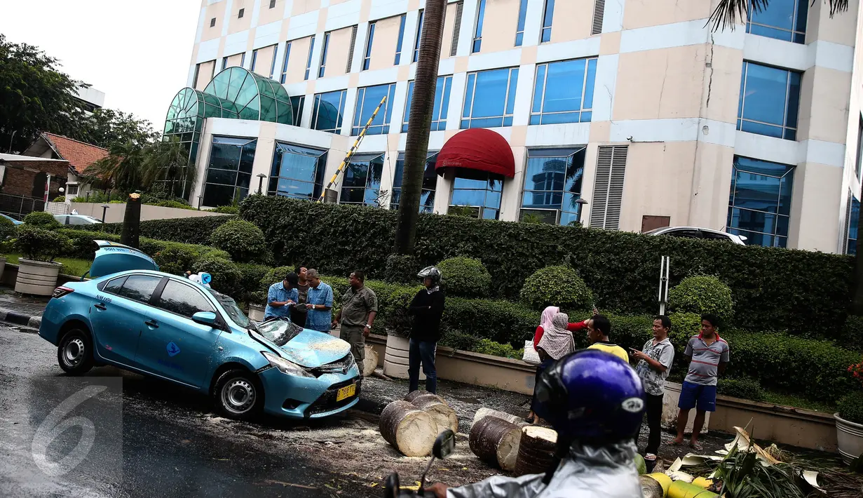 Satu unit taksi ringsek tertimpa pohon tumbang di dekat Hotel Millenium, Jalan Taman Kebon Sirih, Jakarta, Selasa (30/8). Petugas Dinas Pertamanan dan Pemakaman DKI sudah berada di lokasi melakukan penanganan. (Liputan6.com/Faizal Fanani) 