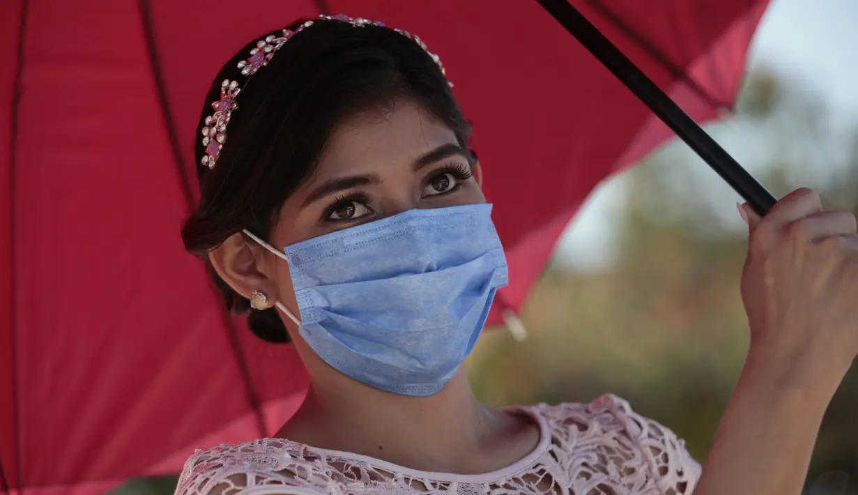 Seorang pengantin perempuan yang mengenakan masker menutupi dirinya dari matahari dengan payung saat pernikahan massal di Managua, Nikaragua, Minggu (14/2/2021). Sekitar 400 pasangan mengatakan "I do" pada Hari Valentine pada acara nikah massal gratis. (AP Photo/Diana Ulloa)