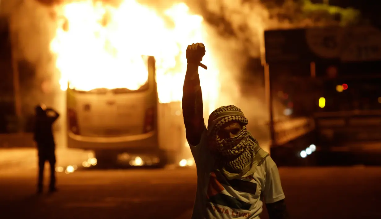 Seorang demonstran berada di dekat bus yang dibakar saat bentrokan dengan polisi dalam unjuk rasa di de Janeiro, Brasil, (29/4). Mereka menentang usulan perubahan undang-undang ketenagakerjaan dan sistem pensiun. (AP Photo/Leo Correa)