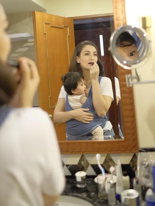 Patut diacungi jempol, peduli dengan penampilan dirinya sendiri namun Atiqah tak meninggalkan perannya sebagai ibu. Sambil merias wajahnya, Salma tetap berada di gendongannya. (Instagram/atiqahhasiholan)