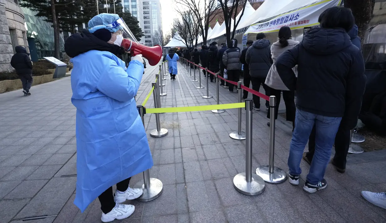 Pekerja medis menggunakan pengeras suara saat orang-orang menunggu tes virus corona di tempat pengujian darurat di Seoul, Rabu (23/2/2022). Kasus harian COVID-19 baru Korea Selatan mencapai rekor tertinggi, melonjak menjadi 171.452 dari 99.569 kasus sehari sebelumnya. (AP Photo/Ahn Young-joon)