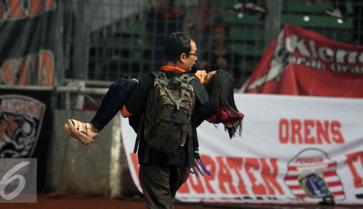 Suporter dievakuasi akibat asap tembakan gas air mata saat kericuhan dengan petugas kepolisian di laga Persija melawan Sriwijaya FC di Stadion GBK Jakarta, Jumat (24/6). Laga dihentikan di menit 81. (Liputan6.com/Helmi Fithriansyah)