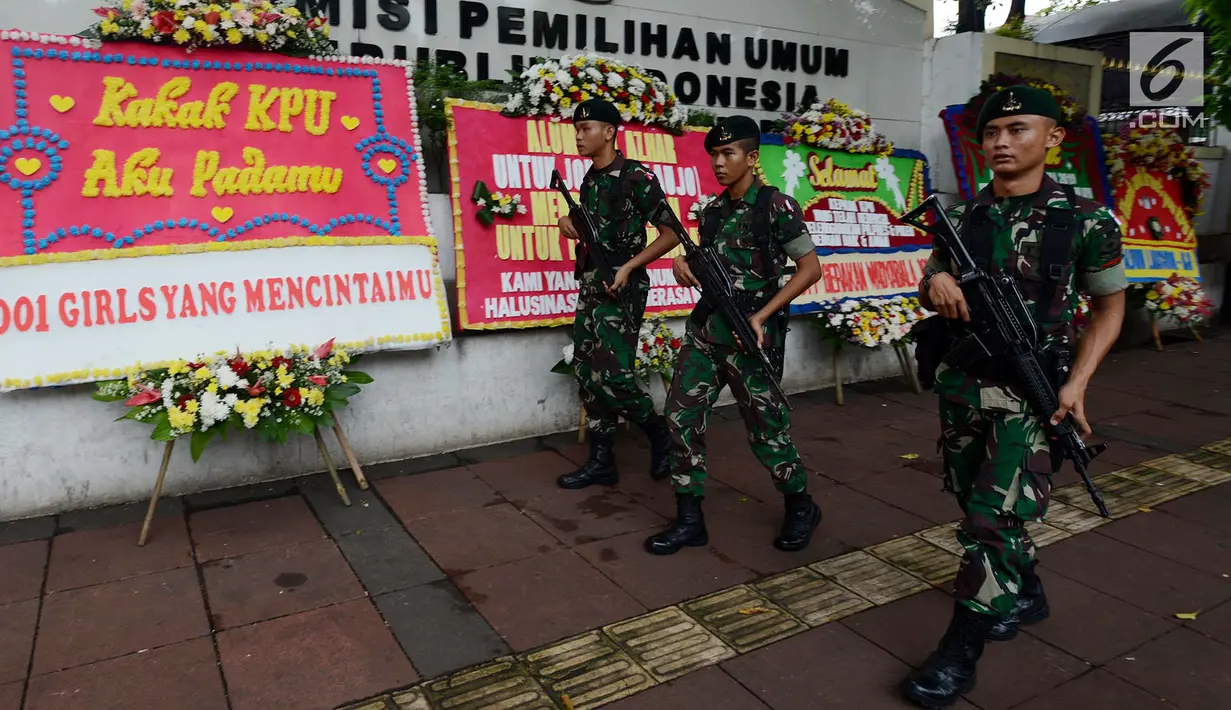 Sejumlah tentara bersenjata berjalan melintasi karangan bunga yang ada di Gedung Komisi Pemilihan Umum (KPU), Jakarta, Sabtu (20/4). Karangan bunga terus berdatangan ke Gedung KPU. (merdeka.com/Imam Buhori)