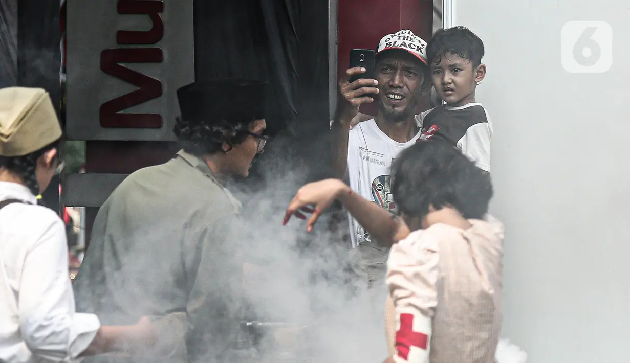 Warga mengambil gambar pertunjukan sosiodrama "Reenactor Bangor" Gelora Bangsa di halaman Museum Naskah Proklamasi Jakarta, Selasa (16/8/2022). Pertunjukan tersebut merupakan salah satu rangkaian acara Napak Tilas Proklamasi dalam rangka menyambut HUT ke-77 Kemerdekaan Republik Indonesia (RI). (Liputan6.com/Faizal Fanani)