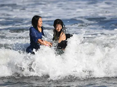 Dua wanita menikmati ombak di sepanjang pantai dekat Pulau Enoshima di pantai Prefektur Kanagawa, barat daya Tokyo (13/8/2019). Enoshima adalah pulau lepas pantai kecil, sekitar 4 km di sekelilingnya, di mulut Sungai Katase yang mengalir ke Teluk Sagami di Prefektur Kanagawa, Jepang. (AFP Photo/Char