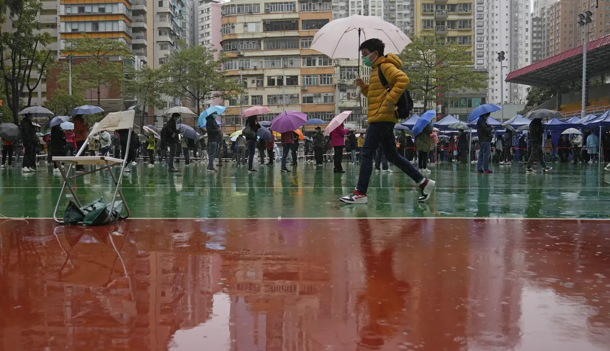 Orang-orang antre tes virus corona di pusat pengujian sementara meskipun hujan di Hong Kong, 22 Februari 2022. Hong Kong akan melakukan pengujian Covid-19 untuk seluruh penduduknya pada Maret mendatang, saat kota itu bergulat dengan wabah terburuk dari varian omicron. (AP Photo/Kin Cheung)