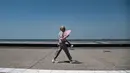 Seorang wanita berjalan di sepanjang tepi pantai Thessaloniki, Yunani utara (23/6/2021).  Yunani bersiap menghadapi gelombang panas pertama musim panas, mendorong suhu siang hari ke wilayah 40+ Celcius di banyak bagian negara. (AFP/ Sakis Mitrolidis)