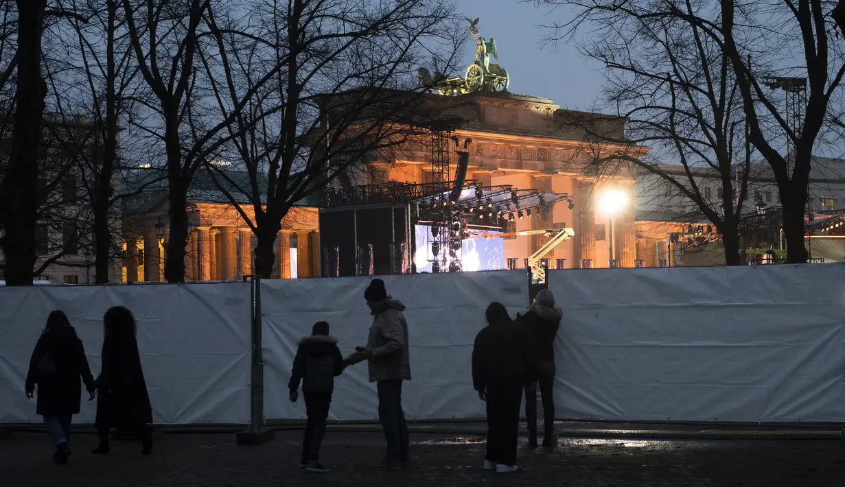 Orang-orang berkumpul di depan pagar saat menyiapkan acara TV di Gerbang Brandenburg di Berlin, Jerman, Rabu (29/12/2021). Perayaan Tahun Baru skala besar telah dibatalkan. (AP Photo/Markus Schreiber)