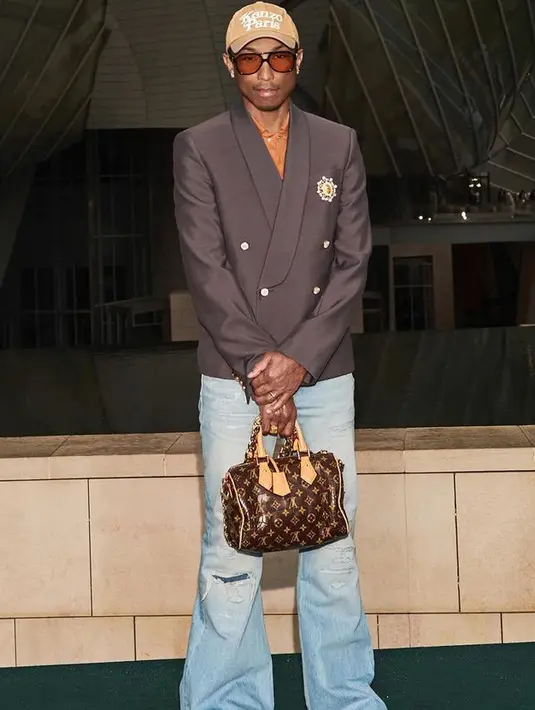 Pharrell William mengenakan blazer oversize dipadukan celana denim flare. Sambil membawa mini bag dari Louis Vuitton. [Louis Vuitton]