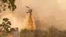 Helikopter menjatuhkan penghambat laju api ke kobaran api dekat Wooroloo, di Perth, Australia, Selasa (2/1/2021). Kebakaran hutan tak terkendali di sebuah wilayah di sebelah timur laut Perth telah menghancurkan puluhan rumah dan kemungkinan mengancam lebih banyak lagi. (Evan Collis/DFES via AP)