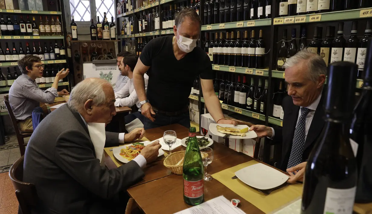 Pramusaji melayani pelanggan di dalam restoran di pusat kota Roma, Italia, Senin (1/6/2021). Mulai Selasa, pelanggan kembali diizinkan mengakses bar dan restoran, yang sebelumnya hanya diizinkan untuk melayani makan di luar ruangan atau takeaway karena pembatasan Covid-19. (AP Photo/Gregorio Borgia)