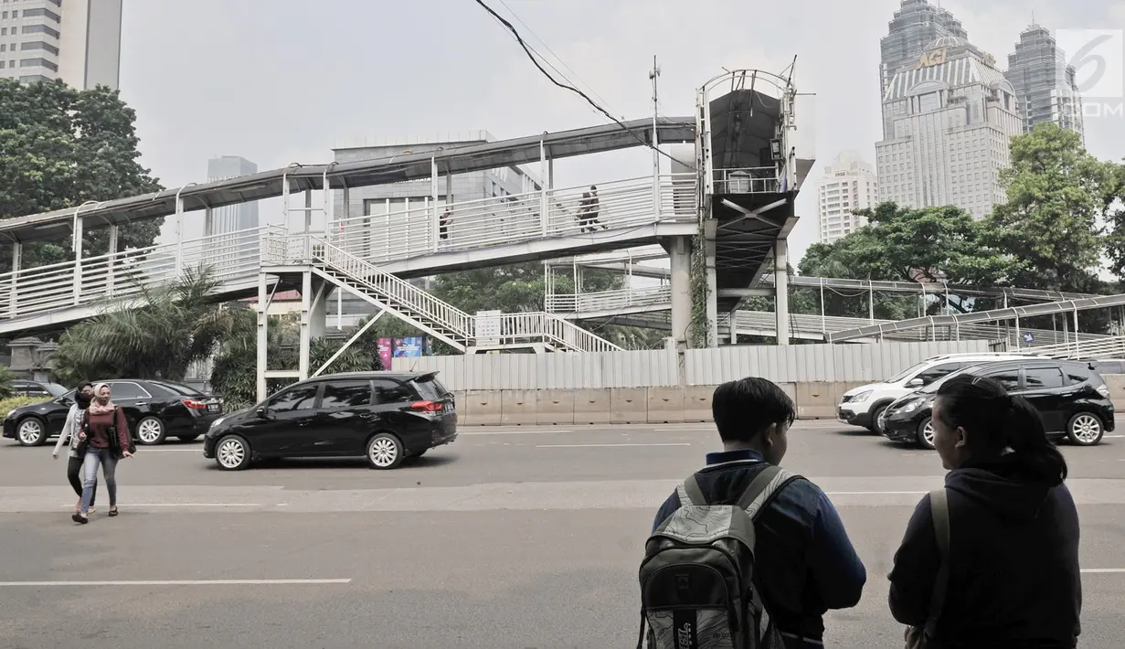 Pejalan kaki saat menunggu sepi lalu lintas sebelum menyeberang ke JPO Polda Metro Jaya, Jakarta, Selasa (8/5). Kondisi JPO Polda Metro Jaya sangat memprihatinkan karena hanya setengah alias buntung. (Merdeka.com/Iqbal Nugroho)