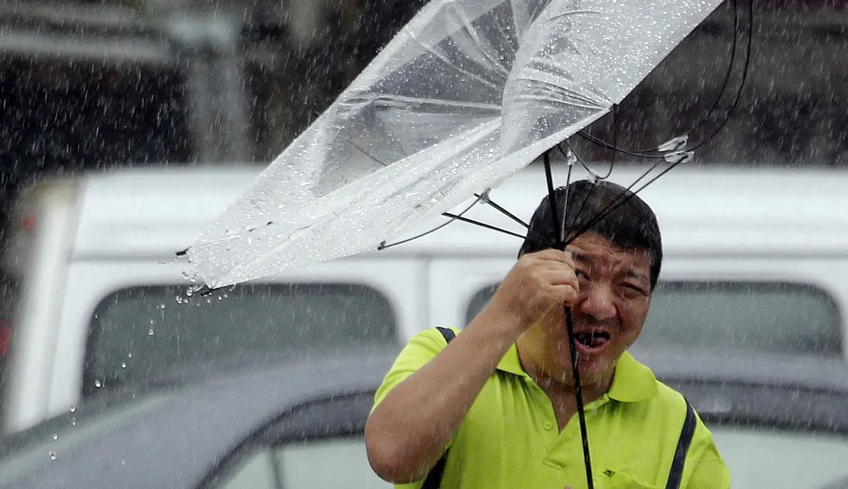 Seorang pria Taiwan memperbaiki payungnya saat melawan angin kencang yang ditimbulkan oleh topan Lekima di Taipei, Taiwan (9/8/2019). Topan Lekima saat ini tengah menghantam Taiwan, membawa angin ribut dengan kecepatan 190 km/jam. (AP Photo / Chiang Ying-ying)