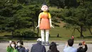 Pengunjung mengambil foto dekat boneka 'Younghee' yang menjadi maskot dalam serial Netflix asal Korea, Squid Game, di Olympic park, Seoul, Selasa (26/10/2021). Boneka setinggi empat meter atau 13 kaki itu, akan dipamerkan di taman tersebut selama tiga bulan. (AP Photo/Lee Jin-man)