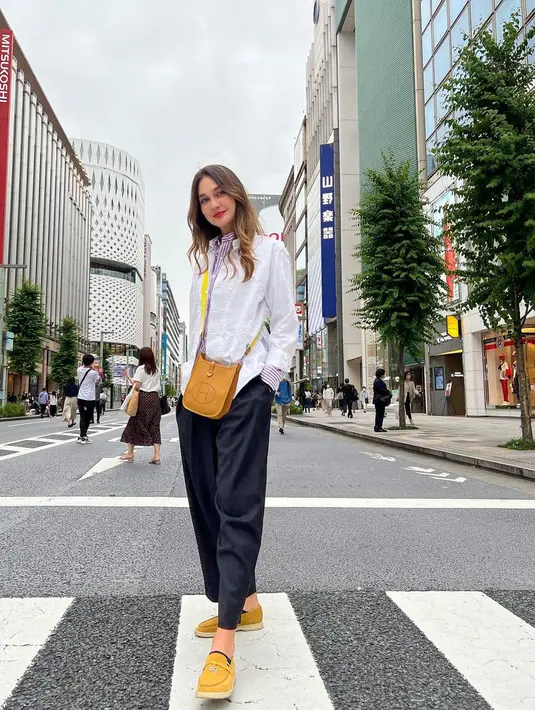 Berlibur di Jepang, Luna Maya tampil berbeda memadukan dua kemeja sekaligus. Ia memadukan kemeja dengan motif striped warna ungu dan putih dengan kemeja berwarna putih polos sebagai outer. Atasannya itu dipadukan dengan celana berwarna hitam, flat shoes, serta sling bag warna kuning, (Instagram/lunamaya).