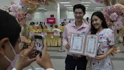 Petugas mengambil gambar pasangan dengan akta pernikahan mereka pada Hari Valentine di distrik Bang-Rak, Bangkok, Thailand, Senin (14/2/2022). Banyak pasangan menikah pada saat ini lokasi karena mereka percaya nama keberuntungannya akan membawa cinta yang tahan lama. (AP Photo/Sakchai Lalit)