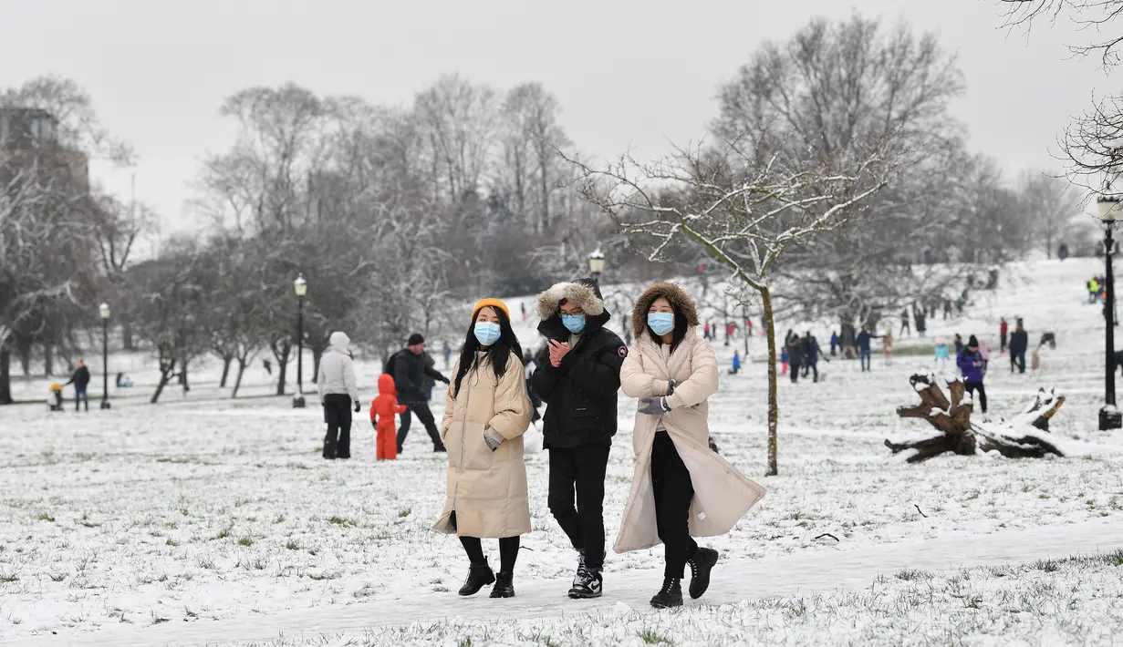 Orang-orang yang mengenakan masker berjalan di atas salju di Primrose Hill di London saat ibu kota mengalami hujan salju yang jarang terjadi pada Minggu (24/1/2021). Hujan salju langka itu membawa kegembiraan di tengah penguncian atau penutupan wilayah (lockdown) secara nasional. (JUSTIN TALLIS/AFP)