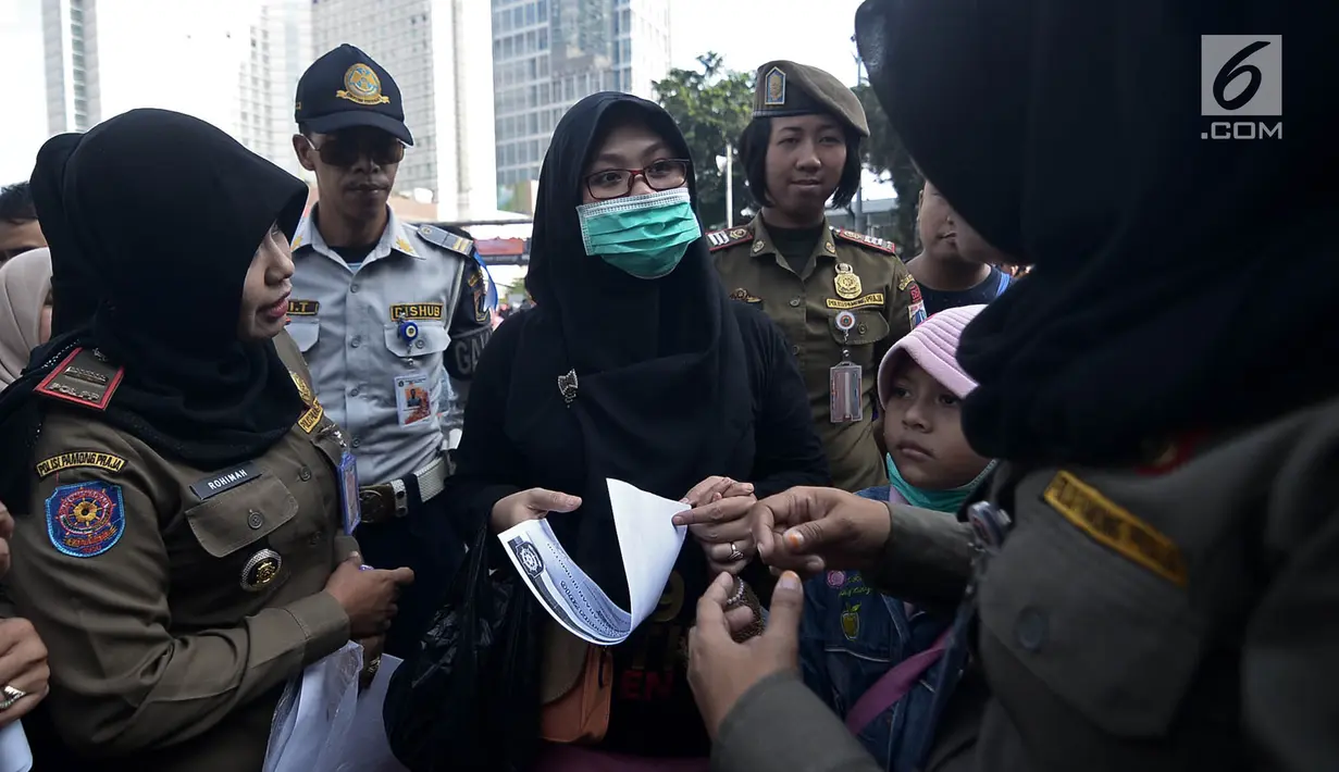 Petugas Satpol PP meminta pengunjung mengganti pakaian bertagline '#2019GantiPresiden' yang dikenakannya selama car free day (CFD), Jakarta, Minggu (6/5). CFD tidak boleh dimanfaatkan untuk kepentingan partai politik dan SARA. (Merdeka.com/Iqbal Nugroho)