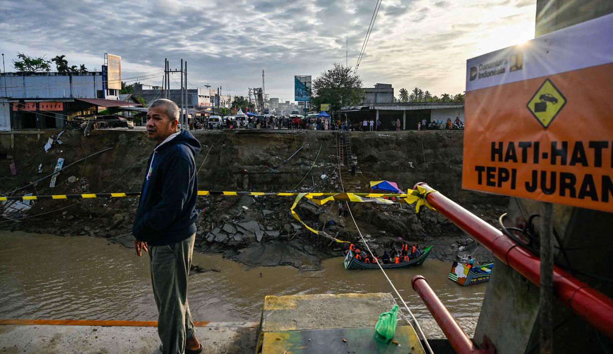 Salah satu sisi jembatan Kuta Blang runtuh akibat banjir bandang yang menerjang wilayah tersebut pada Kamis 27 November 2025 sore hari. Tampak dalam foto, seorang pria menyaksikan dari jembatan yang runtuh di atas Sungai Peusangan di Kuta Blang, Kabupaten Bireuen, Provinsi Aceh, Selasa 9 Desember 2025. (CHAIDEER MAHYUDDIN/AFP)