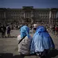 Orang-orang duduk menutupi kepala mereka dari matahari setelah versi kecil dari upacara Pergantian Penjaga berlangsung di luar Istana Buckingham, selama cuaca panas di London, Senin (18/7/2022). Pemerintah Inggris telah mengeluarkan peringatan "merah" pertama mereka untuk panas ekstrem. (AP Photo/Matt Dunham)