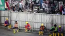 Sejumlah buruh proyek duduk di pintu gerbang dengan latar belakang warga yang sedang beraktifitas saat berlangsungnya Hari Bebas Kendaraan Bermotor (HBKB) di kawasan Bunderan HI, Jakarta, Minggu (24/12). (Liputan6.com/Faizal Fanani)