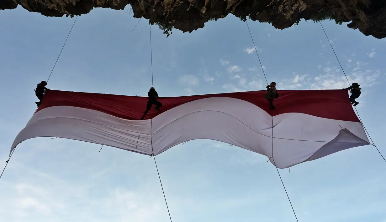 Sekelompok mahasiswa mengibarkan bendera Merah Putih berukuran besar menjelang perayaan Hari Ulang Tahun ke-77 Republik Indonesia di Pantai Lhoknga, Aceh, 16 Agustus 2022. Pengibaran bendera Merah Putih berukuran besar yang dilakukan pada sebuah tebing ini untuk memeriahkan Hari Ulang Tahun ke-77 Republik Indonesia. (CHAIDEER MAHYUDDIN/AFP)