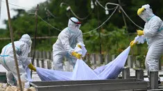 Relawan yang mengenakan pakaian pelindung diri (APD) menurunkan ke dalam kuburan jenazah seseorang yang diduga meninggal akibat virus Corona Covid-19 di sebuah pemakaman, di Yangon (26/10/2020). (AFP/Ye Aung Thu)