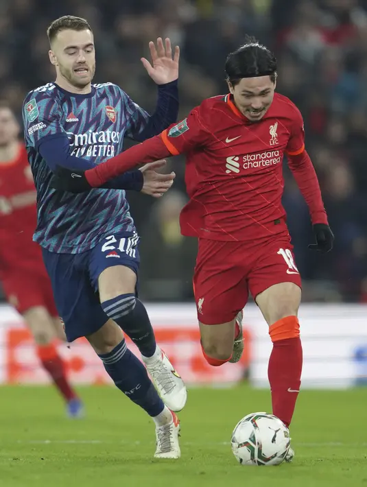 Penyerang Liverpool Takumi Minamino berebut bola dengan bek Arsenal Calum Chambers pada leg pertama semifinal Piala Liga Inggris di Stadion Anfield, Jumat (14/1/2022) dinihari WIB. Arsenal dipkasa bermain imbang tanpa gol oleh Liverpool. (AP Photo/Jon Super)