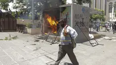Seorang pria melintasi mesin ATM bitcoin bernama Chivo yang dibakar dalam protes terhadap Presiden Nayib Bukele di San Salvador, El Salvador, Rabu (15/9/2021). Ribuan warga Salvador berdemonstrasi menentang bitcoin, yang disahkan sebagai alat pembayaran oleh pemerintah. (AP Photo/Ivan Manzano)