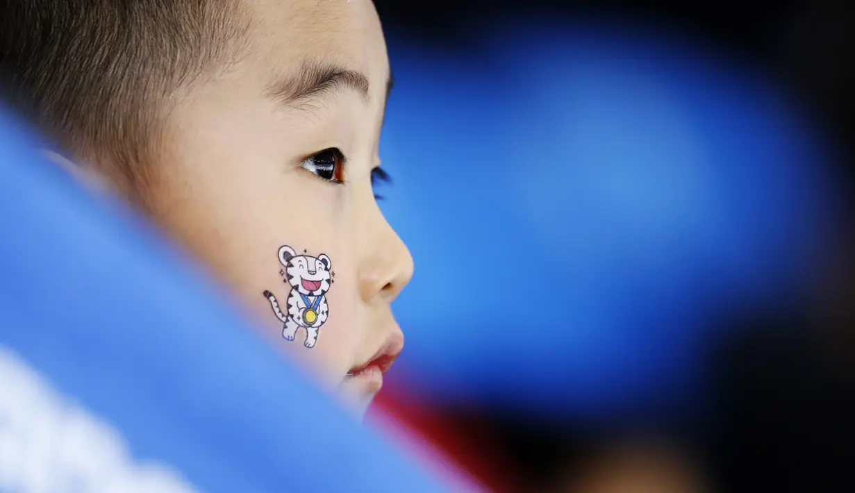 Seorang anak memakai salah satu maskot Olimpiade di wajahnya saat menonton perlombaan speedskating 1.500 meter putri di Gangneung Oval pada Olimpiade Musim Dingin PyeongChang 2018 di Gangneung, Korea Selatan, 12 Februari 2018. (AP Photo/John Locher)