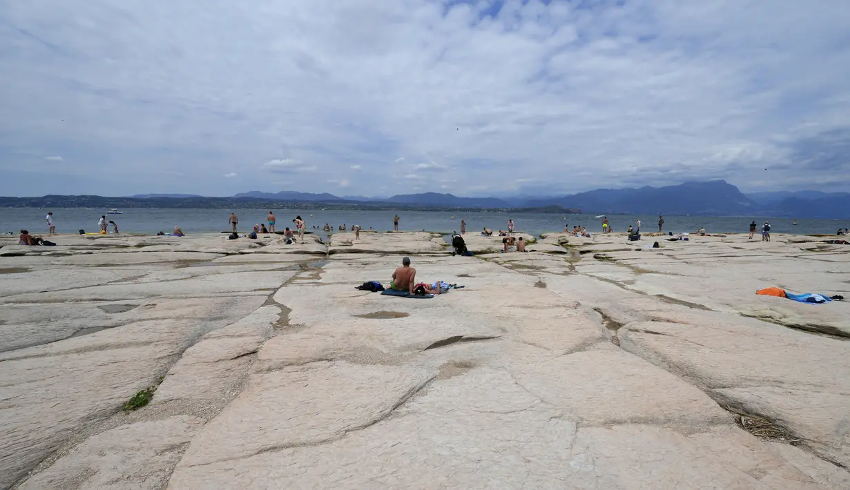 Orang-orang berjemur di semenanjung Sirmione, di danau Garda, Italia, Jumat (12/8/2022). Permukaan air Danau Garda telah turun secara kritis menyusul kekeringan parah yang mengakibatkan munculnya bebatuan di sekitar Semenanjung Sirmione. (AP Photo/Antonio Calanni)