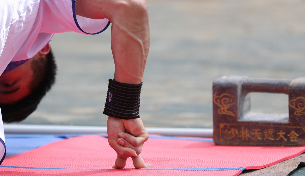 Seorang pria menunjukkan kemampuann push up dengan dua jari pada kompetisi seni bela diri '72 Arts of Shaolin' di kuil Shaolin, Provinsi Henan, China, 30 Juli 2017. Kompetisi ini menampilkan para jago kungfu yang memamerkan kekuatan fisik. (STR AFP)