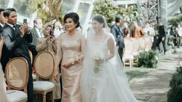 Berjalan menuju altar pernikahan, Mitzi Abigail ditemani sang ibunda sembari pamer senyuman manisnya kepada para tamu undangan. Kebahagiaan Mitzi turut dirasakan oleh netizen karena ikut mengkawal perjalanan cinta Mitzi dan Anthony Ginting selama 10 tahun ini. Aksesori berupa cincin dan kalung membuat penampilan istri Anthony Ginting ini makin cantik. (Liputan6.com/IG/@sinisukanthony)