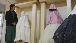 Penjaga toko berdiri di samping manekin dengan kepala tertutup di sebuah toko pakaian perempuan di Herat, Afganistan, pada 5 Januari 2022. Taliban telah memerintahkan pemilik toko di Afghanistan barat untuk memotong kepala manekin, dan bersikeras bahwa patung-patung itu melanggar hukum Islam. (AFP)
