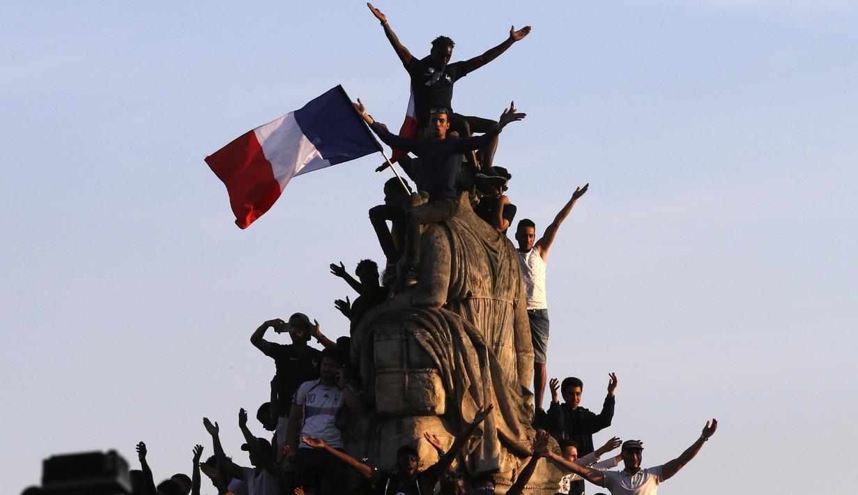 Fans memanjat patung Place de la Concorde saat menyambut timnas Prancis di Champs-Elysee avenue, Paris, (16/7/2018). Prancis berpesta merayakan keberhasilan Les Bleus meraih trofi Piala Dunia 2018. (AP/Bob Edme)