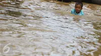 Seorang anak bermain di tengah jalan permukiman Bukit Duri, Jakarta yang terendam banjir, Kamis (16/2). Meluapnya Bendungan Katulampa, Bogor, menyebabkan permukiman kawasan Bukit Duri tergenang air dengan ketinggian 10 - 80 cm. (Liputan6.com/Helmi Afandi)