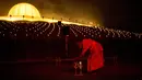 Biksu Buddha menyalakan lilin selama perayaan Makha Bucha, di Wat Dhammakaya, utara Bangkok, Jumat (26/2/2021). Saat perayaan Makha Bucha, penganut Buddhisme di Thailand akan berkunjung ke kuil pada malam hari untuk mengikuti upacara cahaya lilin yang dikenal sebagai wien tien. (Jack TAYLOR/AFP)