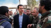 Presiden Suriah Bashar al-Assad berbincang dengan pasukan pemerintah di garis depan wilayah Ghouta Timur, Minggu (18/3). Ini adalah pertama kalinya Assad mengunjungi daerah ini selama bertahun-tahun. (HO/SYRIAN PRESIDENCY FACEBOOK PAGE/AFP)