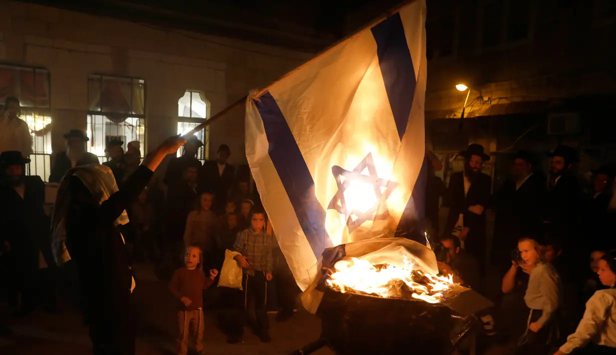 Seorang Yahudi ultra ortodoks antizionis membakar bendera Israel di Yerusalem ultra-Ortodoks Mea Shearim, Rabu (2/5). Upacara ini menandai peringatan kematian Rabbi Talmudic Rabbi Shimon Bar Yochai sekitar 1.900 tahun lalu. (MENAHEM KAHANA / AFP)